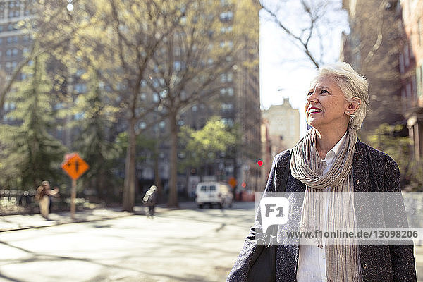 Nachdenkliche ältere Frau lächelt auf der Straße in der Stadt