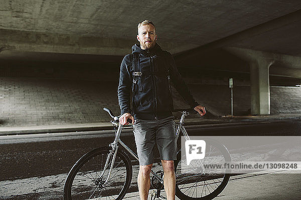 Porträt eines selbstbewussten männlichen Pendlers  der mit dem Fahrrad auf der Brücke steht