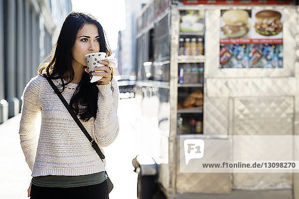 Junge Frau trinkt Kaffee aus Einwegglas mit Konzessionsstand im Hintergrund