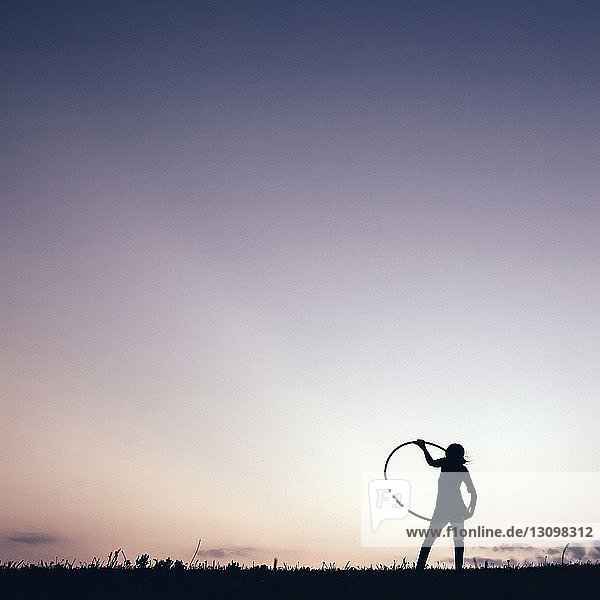 Silhouettenmädchen spielt mit Hula-Hoop-Reifen vor klarem Himmel