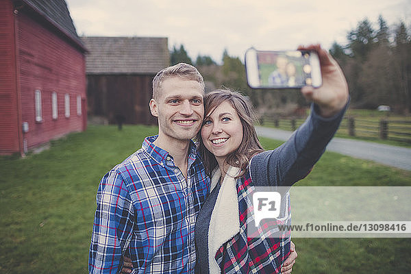 Glückliches Paar  das sich im Stehen auf einem Grasfeld ein Selfie nimmt
