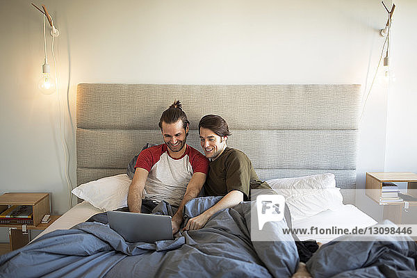 Homosexuelles Paar benutzt Laptop-Computer  während es sich zu Hause im Bett entspannt
