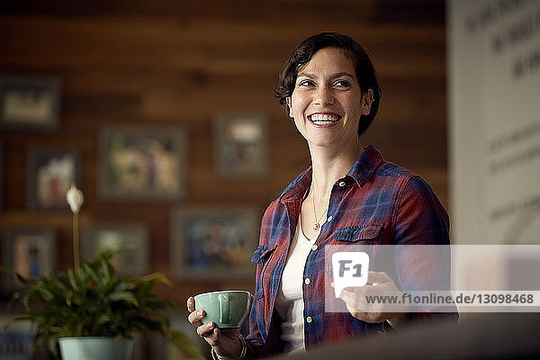 Low angle view of happy woman holding coffee cup while standing in cafe
