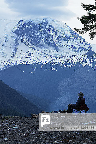 Mann sitzt auf Stuhl und schaut auf schneebedeckten Berg