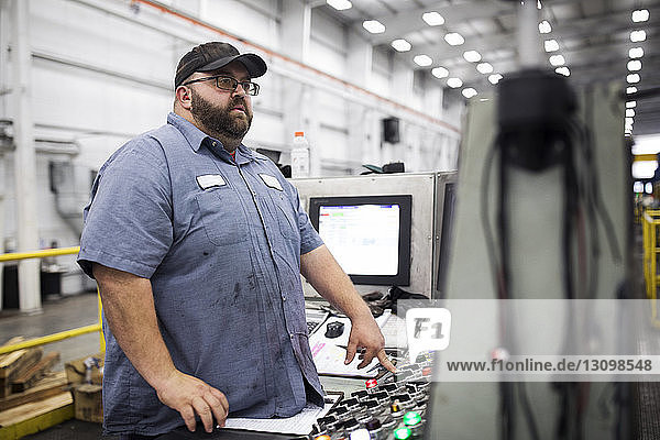 Arbeiter  der während der Arbeit in einer Fabrik der Stahlindustrie an einer Maschine steht