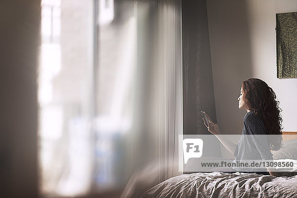 Frau benutzt Mobiltelefon  während sie zu Hause im Bett sitzt