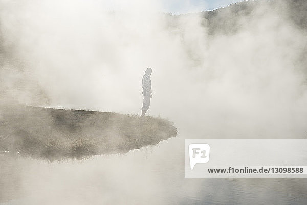 Seitenansicht eines Mannes  der am Geysir inmitten von Dampf im Yellowstone-Nationalpark steht
