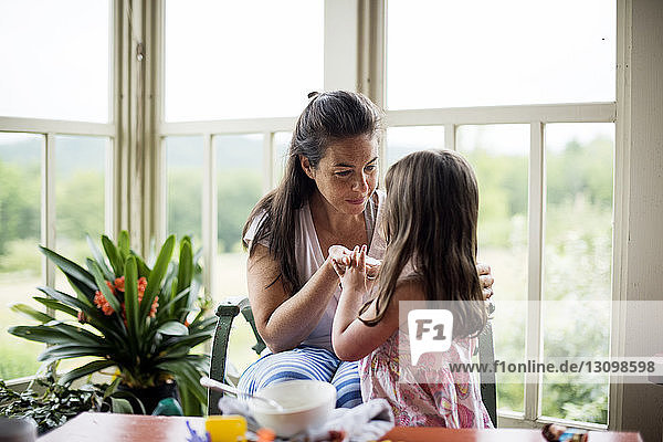 Mother talking with daughter sitting on chair by window at home
