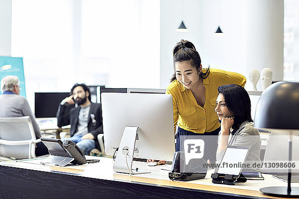 Businesswomen working on desktop computer with male colleagues sitting in back ground