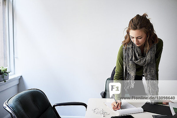 Geschäftsfrau schreibt auf Buch  während sie am Konferenztisch im Sitzungssaal steht