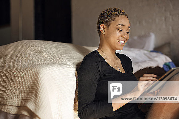 Glückliche junge Frau benutzt Tablet-Computer im Schlafzimmer
