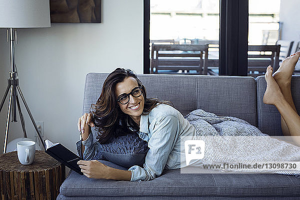 Woman looking away while reading book on sofa at home