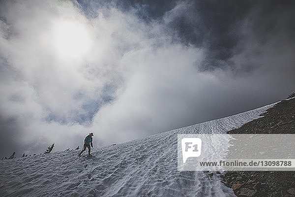 Low angle view of female hiker hiking on snow against cloudy sky