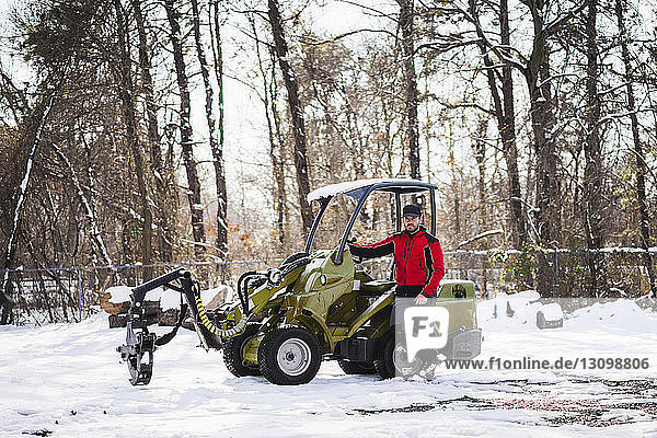 Porträt eines Arbeiters  der auf einem Fahrzeug auf einem schneebedeckten Feld im Hinterhof steht