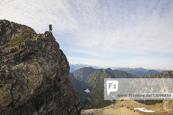 Low angle view of carefree hiker standing on mountain against cloudy sky
