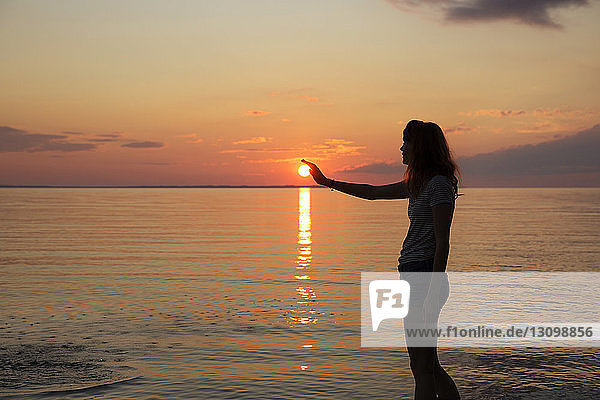 Silhouette eines Teenager-Mädchens  das die Sonne berührt  während es am Strand steht