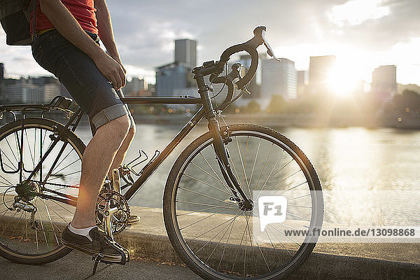 Niedriger Abschnitt eines Mannes  der bei Sonnenuntergang auf der Straße am See Fahrrad fährt