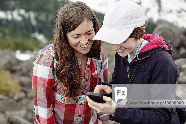 Happy female friends using mobile phone while standing on mountain
