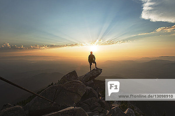 Man standing on rock at cliff against sky during sunset