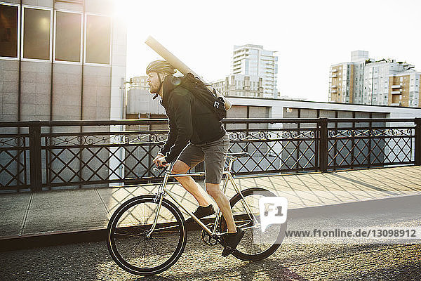 Männlicher Pendler in voller Länge mit Rucksack fährt Fahrrad auf Brücke gegen Himmel