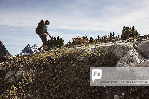Seitenansicht eines Mannes beim Wandern mit Hund auf einem Berg gegen den Himmel