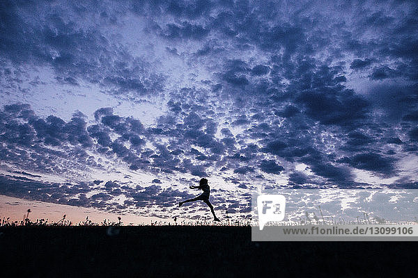 Silhouettenmädchen springt auf Feld gegen dramatischen Himmel