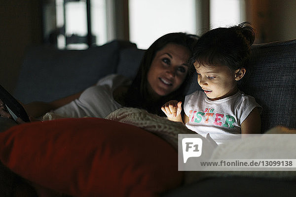 Frau sieht Tochter an  die zu Hause einen Tablet-Computer benutzt