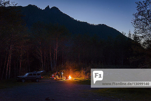 Hiker camping by campfire against mountains during dusk
