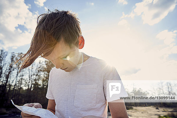 Junge liest Zeitung  während er bei strahlendem Sonnenschein am Berg Arabia gegen den Himmel steht