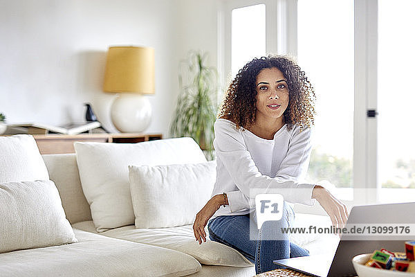 Portrait of woman with laptop computer sitting on sofa at home