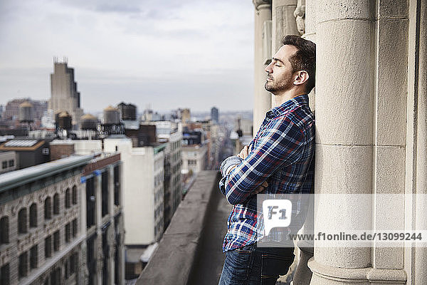 Man leaning on column at balcony against cityscape