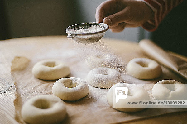 Geschnittene Hand einer Frau  die zu Hause in der Küche Mehl auf Donut-Teig streut