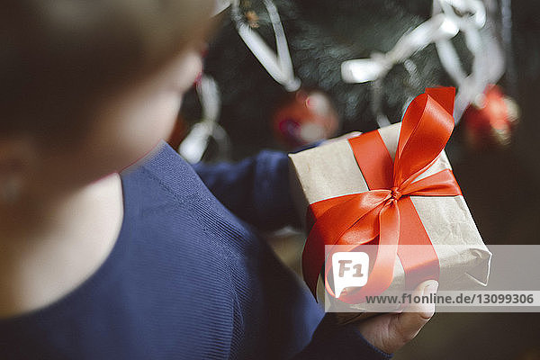 Close-up of boy holding gift by Christmas Tree at home