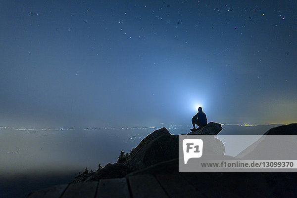 Scherenschnitt eines Mannes  der in der Nacht im Mount Pilchuck State Park auf Felsen gegen den Himmel sitzt