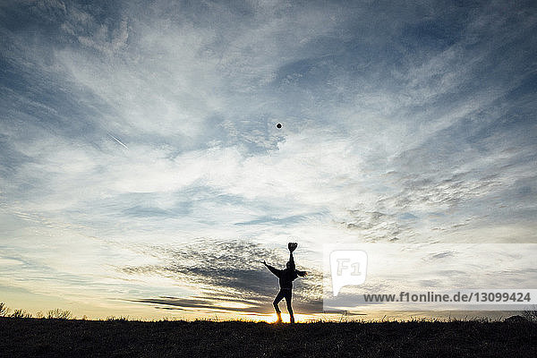 Silhouettenmädchen spielt bei Sonnenuntergang mit Ball gegen den Himmel