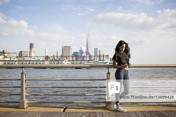 Frau telefoniert am Geländer mit Manhattan im Hintergrund