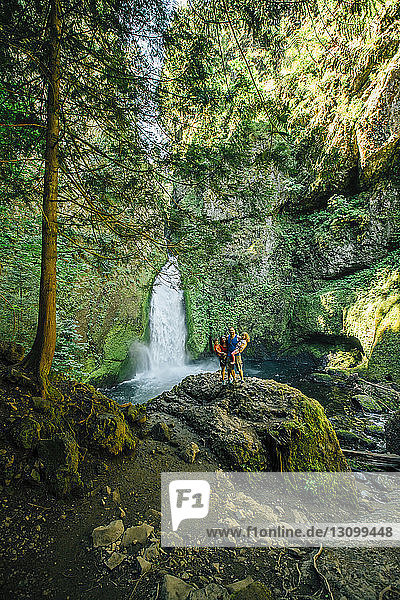 Familie steht auf Felsen gegen Wasserfall im Wald