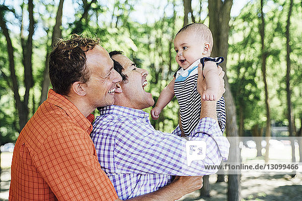 Smiling homosexual couple playing with baby boy at beach