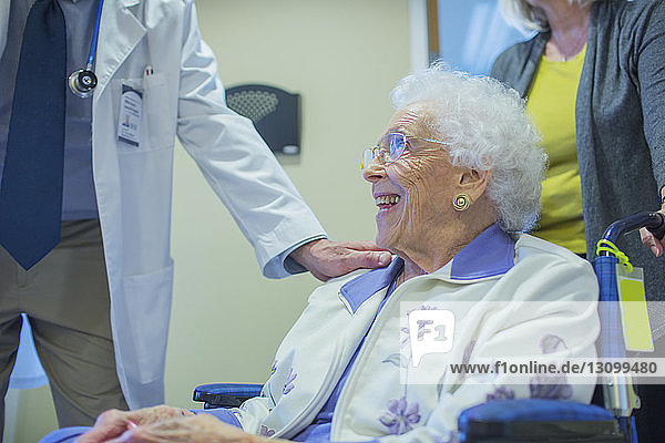 Männlicher Arzt steht neben lächelnder Patientin im Rollstuhl auf der Krankenhausstation