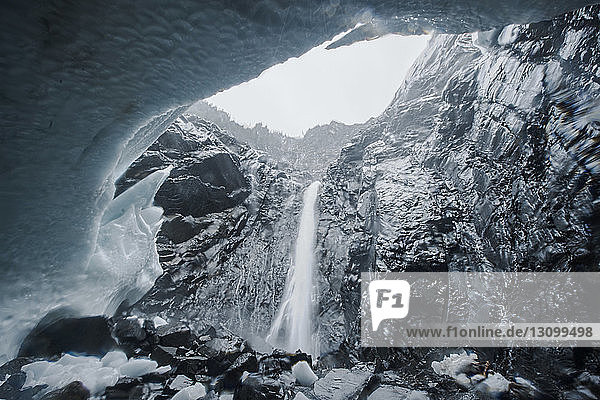 Niedrigwinkelansicht des Wasserfalls gegen den Himmel durch eine Eishöhle gesehen