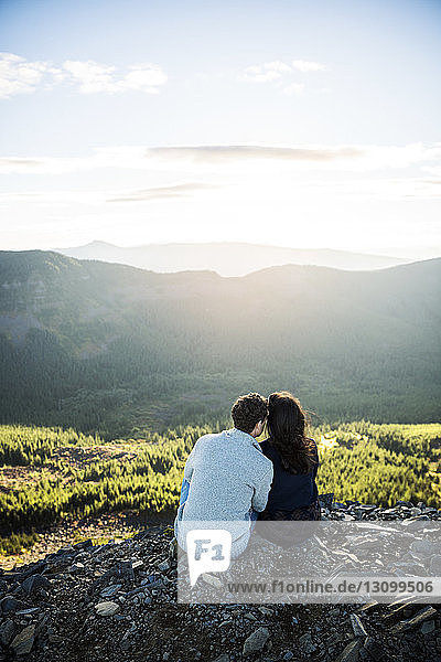 Rückansicht eines Paares  das auf einem Felsen gegen Berge sitzt