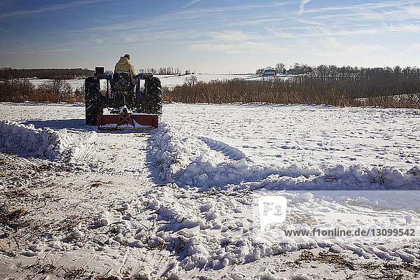 Man driving tractor on snow covered field against sky