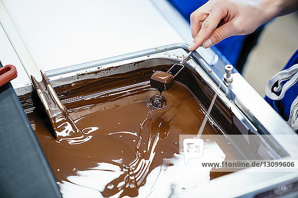 Geschnittene Hand einer Köchin  die Schokolade mit der Gabel in Fondue taucht