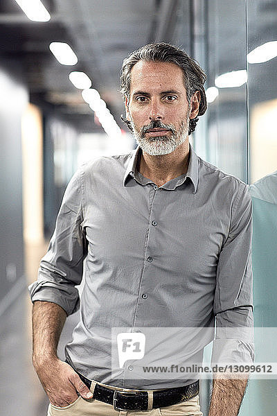 Portrait of confident businessman with hand in pocket standing in office lobby