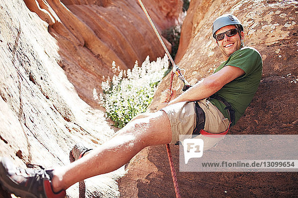 Low angle view of smiling man climbing mountain with rope