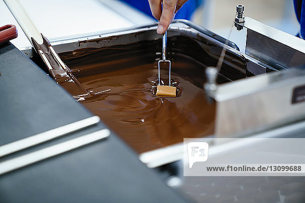 Abgehackte Hand einer Köchin  die in der Fabrik Schokolade mit der Gabel in Fondue taucht