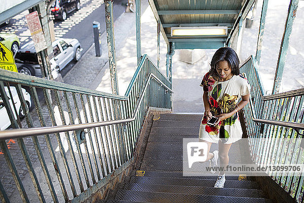 High angle view of woman using phone while moving up on steps
