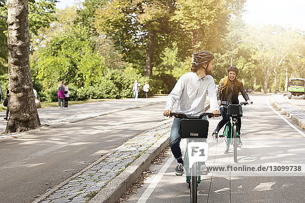 Happy couple riding bicycle on road in park