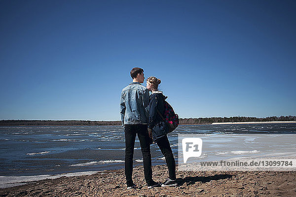 Couple standing at beach against clear blue sky during sunny day