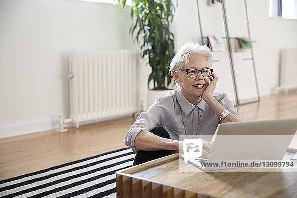 Ältere Geschäftsfrau benutzt Laptop  während sie im Büro auf einem Teppich sitzt